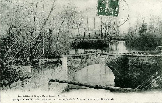 Ein altes Schwarz-Weiß-Foto einer baufälligen Brücke über einen Fluss, mit Bäumen auf beiden Seiten, einem Stempel oben und Text unten.