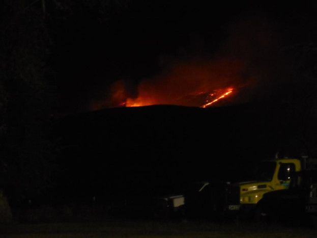 Ein Fahrzeug parkt nachts mit einem Feuer im Hintergrund.