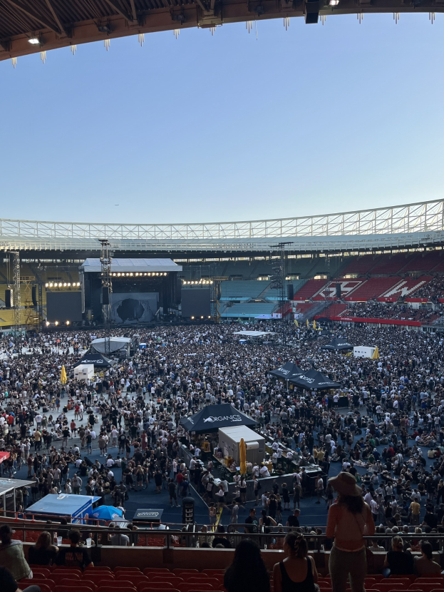 Große Menge sitzend und stehend in einem Stadion mit Zelten, Geländern und Überdachung während eines Konzerts in der O2 Arena in London.
