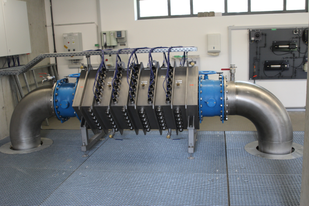 Eine große Wärmetauscher-Maschine in einem Gebäude mit einem Boden, einer Wand und Fenstern, die mit verschiedenen Komponenten und Kabeln verbunden ist.