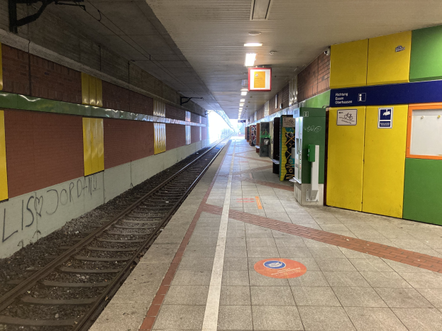 Ein Bahnsteig in Berlin Hauptbahnhof, Deutschland, mit einem Zug auf den Schienen, beleuchtet von Deckenleuchten, einer Graffiti-bedeckten Wand auf der linken Seite und ein paar Gegenständen auf der rechten Seite.