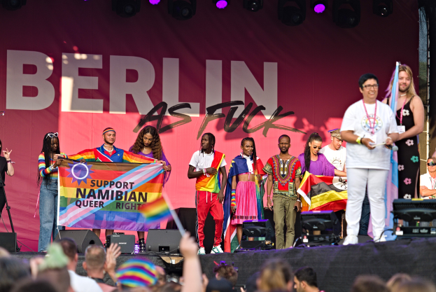 Gruppe von Menschen auf einer Bühne mit einem Banner 'Berlin as Fuck', Lautsprechern, Mikrofonen und einer Menge mit erhobenen Händen unten.