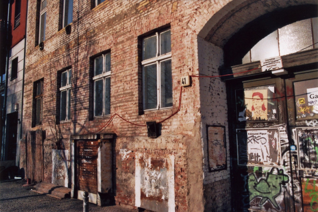 Altes Backsteingebäude mit Graffiti, Fenstern, Türen, Rohren und einer Straße unten.