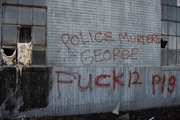 Graffiti auf einer Gebäudewand mit der Aufschrift "Polizei Mord George Fuck 12 P19" mit Fenstern und verstreuten Gegenständen davor.