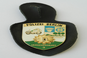 Ein schildförmiges Polizeibadgebnis mit "Polizei Berlin" in schwarzer fetter Schrift auf einem blauen Hintergrund mit einem weißen Stern und einem weißen Rand, das auf einer Oberfläche liegt.