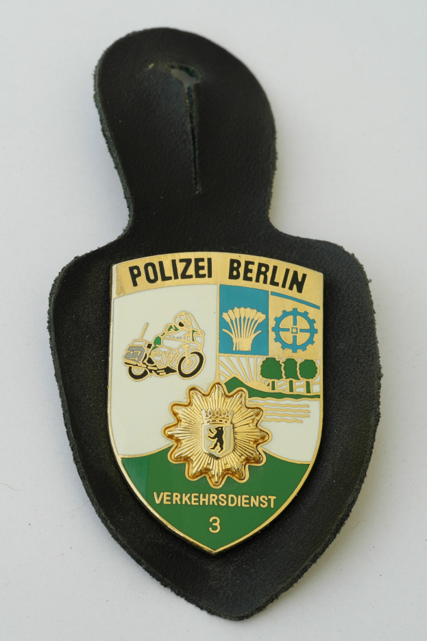 Ein schildförmiges Polizeibadgebnis mit "Polizei Berlin" in schwarzer fetter Schrift auf einem blauen Hintergrund mit einem weißen Stern und einem weißen Rand, das auf einer Oberfläche liegt.