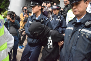 Eine Gruppe von Polizeibeamten steht vor einer Menge mit Kameras, im Hintergrund ein Gebäude mit Säulen und Deckenlampen.