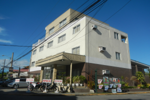 Wohnanlage mit parkenden Autos, Schildern, Strommasten, Bäumen und einem bewölkten Himmel.