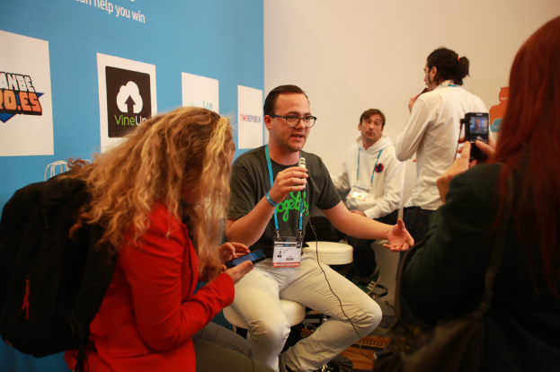 Ein Interview mit Menschen mit Mikrofonen und einer Kamera, ein Banner ist links zu sehen und es gibt Menschen in der Mitte und im Hintergrund.