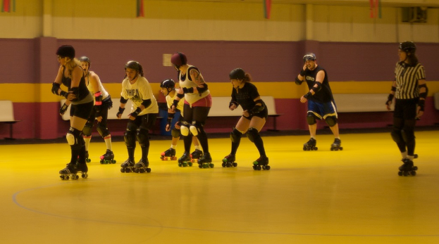 Leute in Kleidung sind auf einem Boden mit Bänken vor einer Wand Schlittschuhlaufend.