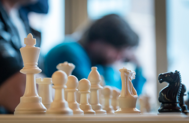 Ein Schachbrett mit Figuren und einigen Personen im Hintergrund.