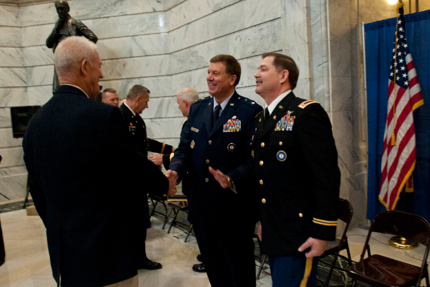 Menschen sch√ľtteln sich in einem Raum mit Stühlen, einer Statue neben einer Wand, einer Flagge und einem Vorhang auf der rechten Seite die H√§nde.