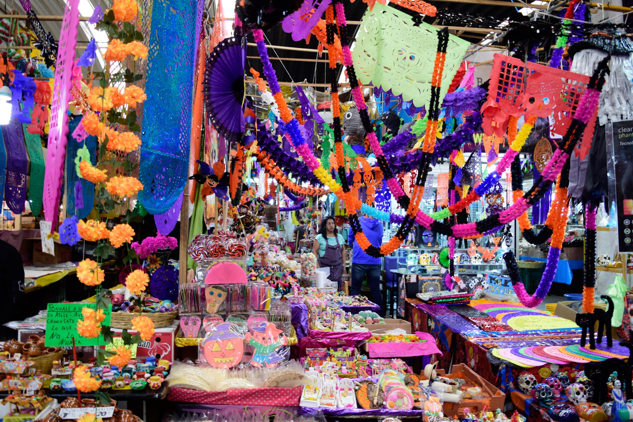 Ein belebter Markt mit Ständen, die Spielzeug, Dekorationsartikel und andere Gegenstände verkaufen, unter einer Decke, die mit Lichtern geschmückt ist, mit Menschen, die umherlaufen.