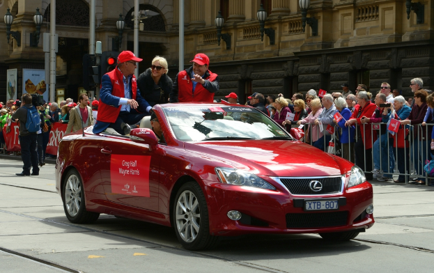Menschen in einem Auto auf einer Straße mit verschiedenen Objekten, Schildern und Menschen im Hintergrund.
