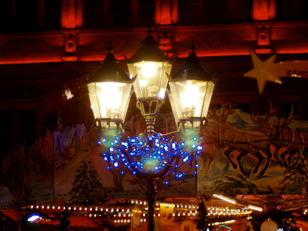 Eine Straßenlaterne in einer Stadt in der Nacht, geschmückt mit Lichtern und Dekorationen, steht vor einem Gebäude und verbreitet eine festliche Atmosphäre.