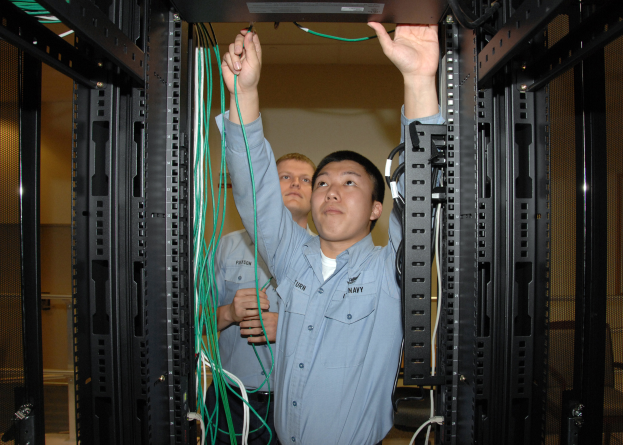 Zwei Männer bei der Arbeit an einem Server in einem Rechenzentrum, umgeben von Kabelregalen und einer Wand im Hintergrund.