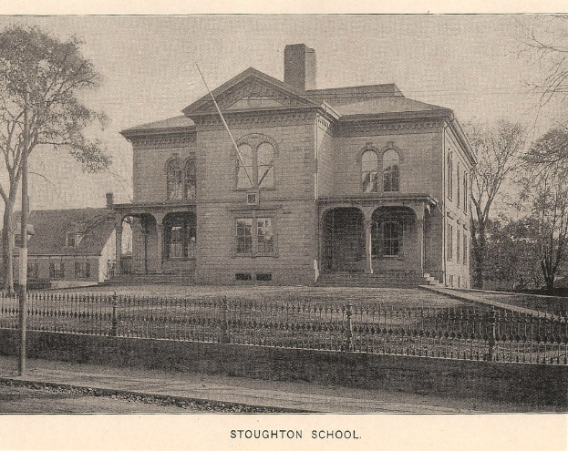 Ein Zaun mit Pfählen, Bäumen und Gebäuden im Hintergrund.