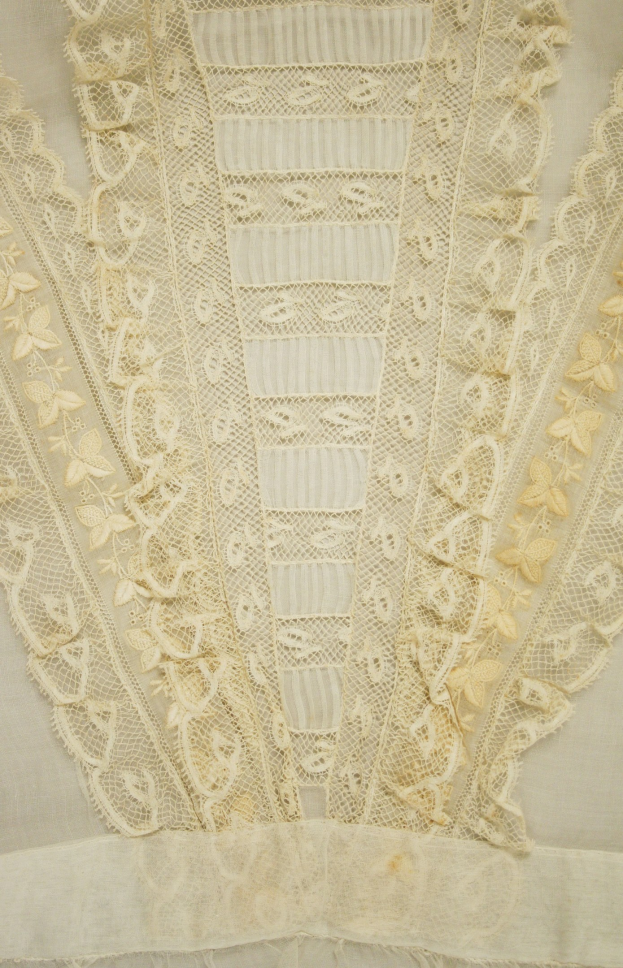 Nahaufnahme eines weißen Kleides mit zarter, detailreicher Spitzenverzierung in verschiedenen Formen und Mustern aus leichtem, luftigem Sommergewebe.