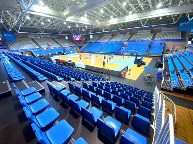 Eine große Hallenarena in Sarajevo, Bosnien und Herzegowina, mit einem Basketballfeld und einigen Menschen, blauen Stühlen auf beiden Seiten und einer Decke mit Lampen und Trägern.