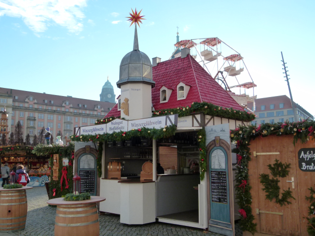 Ein kleines Gebäude mit rotem Dach und einem Riesenrad davor, umgeben von Menschen und Festdekorationen bei einem Oktoberfest in München, Deutschland.