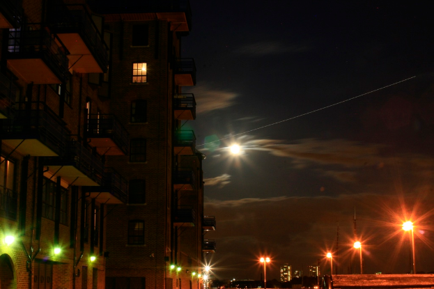 Eine nächtliche Aufnahme eines Gebäudes mit vielen Fenstern und Balkonen, mit Straßenlaternen auf der rechten Seite.
