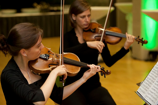 Zwei Männer spielen Geige mit einem Buch vor sich.