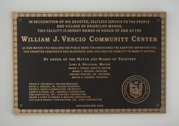 Schwarzes rechteckiges Schild mit weißer, fetter, zentrierter Schrift, die "William J. Vesco Community Center" lautet, an einer Gebäudewand angebracht.