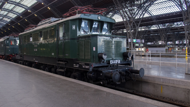 Ein Zug auf den Schienen mit Geländern und Brettern im Hintergrund, Lichter auf dem Dach und ein Himmel darüber, mit einem Boden darunter.