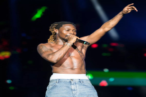 Travis Scott performt auf der Bühne beim Coachella Valley Music and Arts Festival, hält ein Mikrofon und ist von hellen Lichtern umgeben mit einem unscharfen Hintergrund.