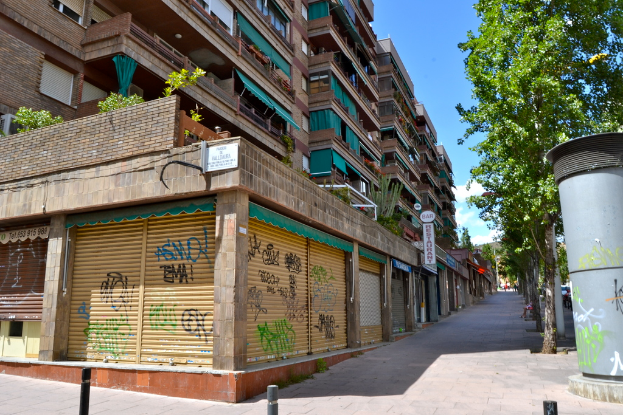 Eine Szene mit Gebäuden mit Fenstern, grünen Kleidungsstücken, Geschäften, Schildern und umliegenden Bäumen und Pflanzen.