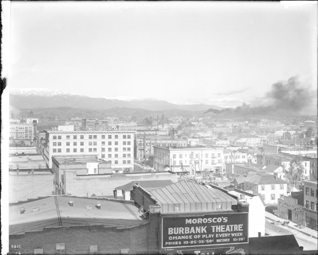Ein Schwarz-Weiß-Bild eines Fabrikgebäudes mit Rauch, der aus seinem Schornstein aufsteigt, umgeben von anderen Gebäuden.
