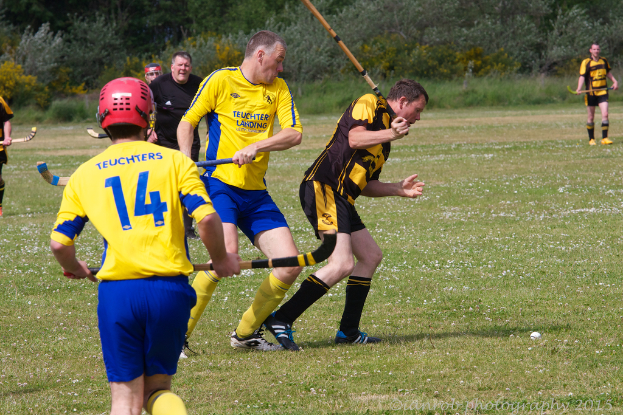 Menschen spielen Hockey auf einem grünen Feld mit anderen und Grünflächen im Hintergrund.