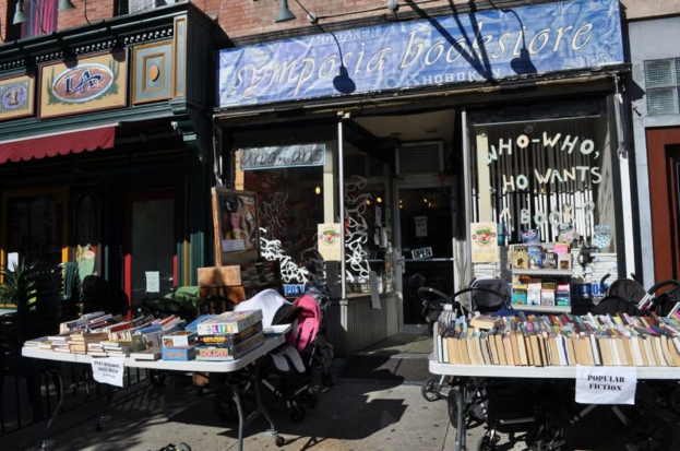 B├╝cher und Papiere auf Tischen mit St├╝hlen, Gesch├Ąften, Brettern und Lichtern im Hintergrund.