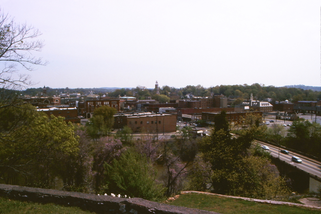 Eine Stadtansicht mit Gebäuden, Bäumen, Pfählen, Straßen, Fahrzeugen und Himmel.
