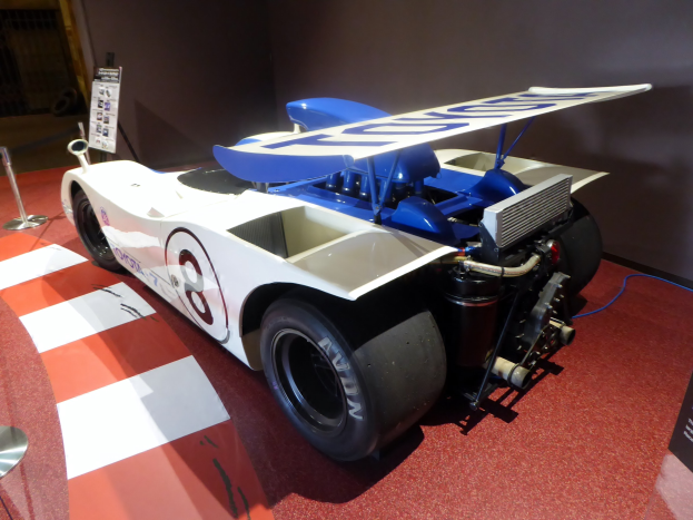 Ein weißes und blaues Rennauto in einem Museums-Setting auf dem Goodwood Festival of Speed, umgeben von Barrieren und Informationsschildern.