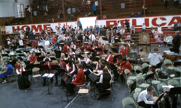 Eine Gruppe von Kindern sitzt auf Stühlen in einem Stadion bei einer Musikstunde, im Hintergrund sind Stadionplätze zu sehen.