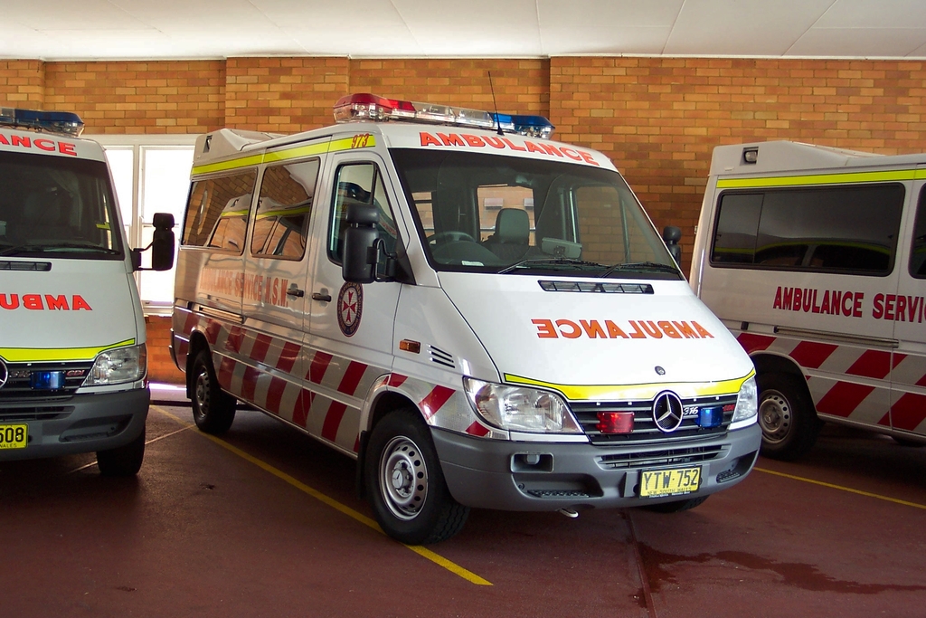 Ein weißer Rettungswagen steht in der Mitte des Bildes, mit einer Backsteinwand im Hintergrund.
