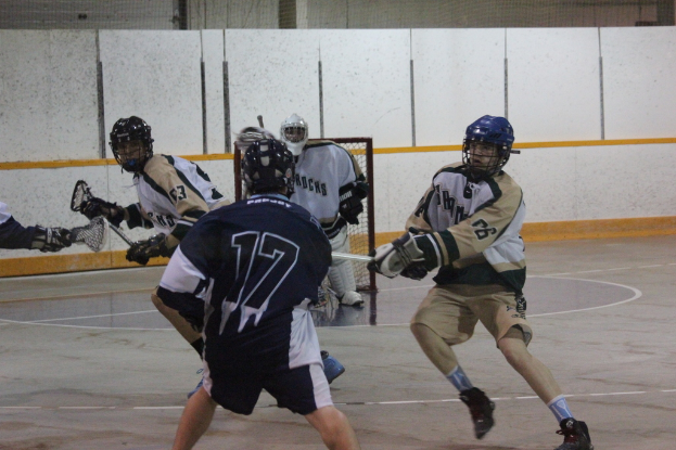Menschen in Helmen mit Stöcken scheinen in einem Innenraum mit einem Netz im Hintergrund zu kämpfen.
