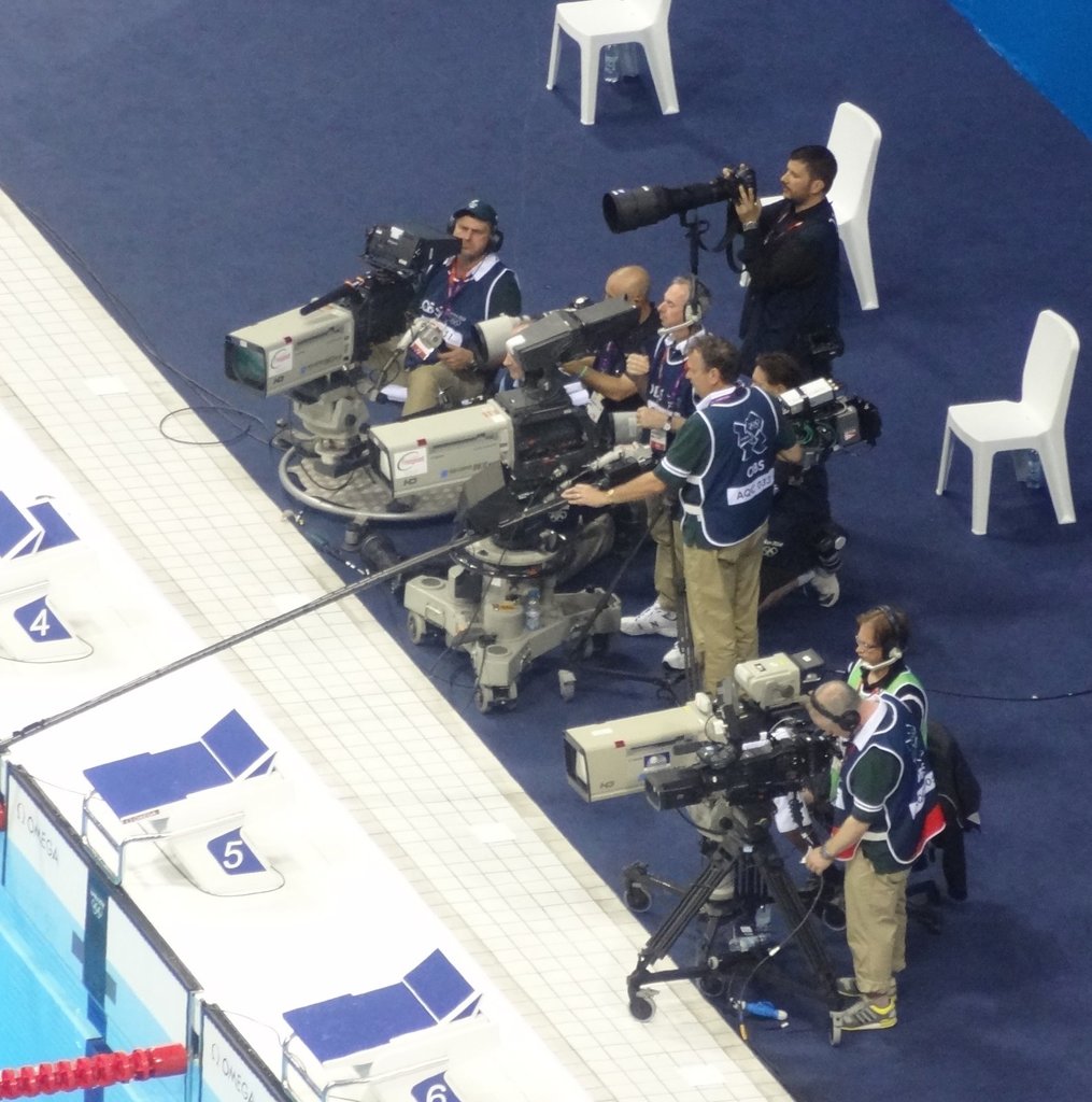 Mehrere Personen mit Kameras, im Hintergrund sind einige Stühle zu sehen.