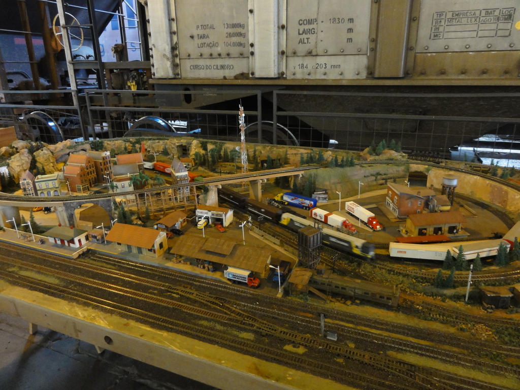 Eine Miniaturlandschaft auf einem Tisch mit einer Schienenstrecke, einem Zug, Gebäuden, Fahrzeugen, einer Brücke, einem Turm und Bäumen.