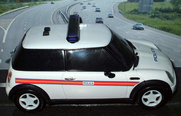 Weißer Polizeiwagen mit "Polizei" Aufschrift auf einer Straße außerhalb der Stadt, umgeben von Verkehr, Gras und Bäumen auf beiden Seiten.