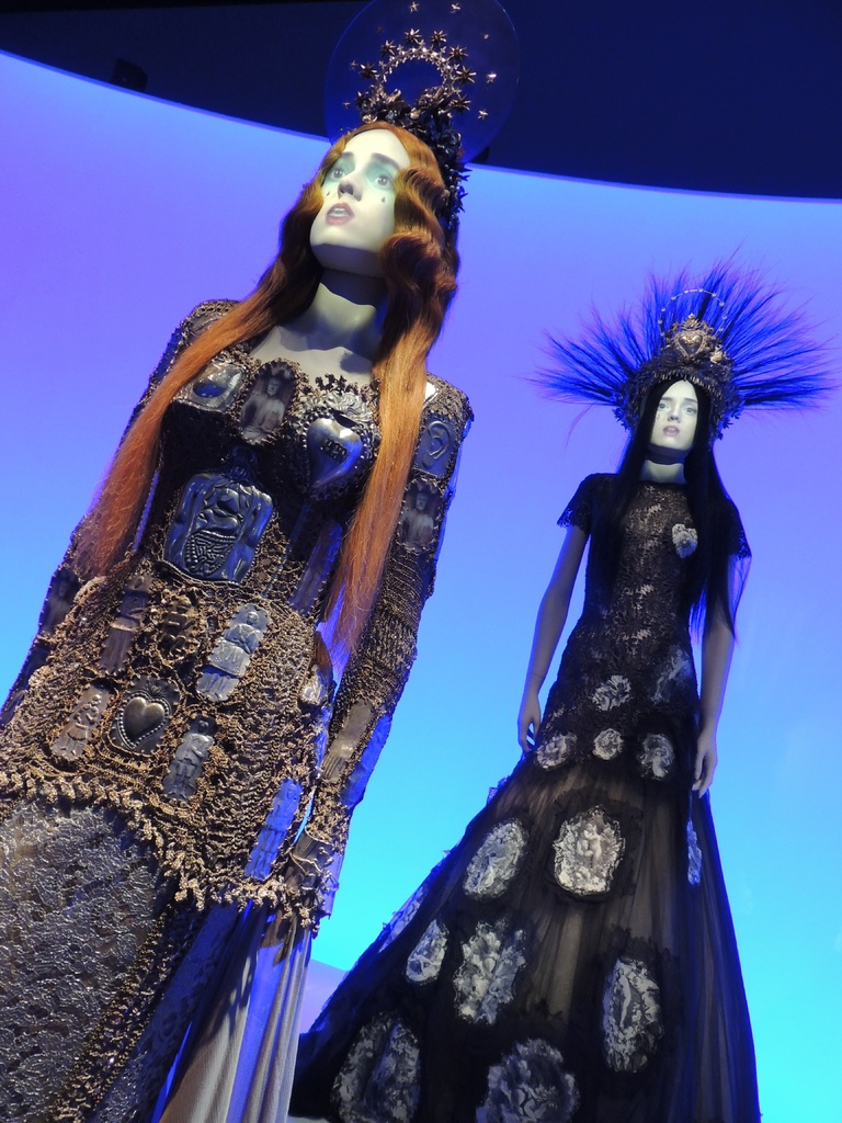 Zwei Schaufensterpuppen in verschiedenen Kleidern und Kopfbedeckungen in einem Geschäft.