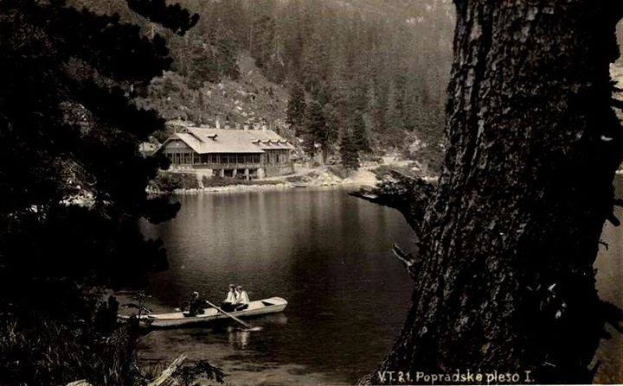Ein Schwarz-Weiß-Foto von zwei Menschen in einem Kanu auf einem See in Popradskie, Polen, umgeben von Bäumen und einem Haus im Hintergrund, aufgenommen in den 1920er Jahren.