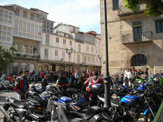 Ein cremefarbenes Gebäude mit zahlreichen Fenstern, das an ein Backsteingebäude mit einer Metallbalustrade angrenzt, mit mehreren geparkten Fahrrädern und Menschen, die davor stehen und sich unterhalten.
