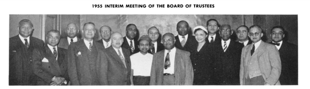 Eine Gruppe von Männern in Anzügen lächelt und steht zusammen vor einer Wand, mit Text oben und unten, der '1955 Zwischenversammlung des Kuratoriums' in Schwarzweiß zeigt.