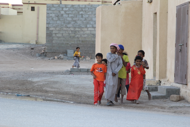 Eine Gruppe lachender Kinder, die draußen vor Gebäuden, Wasser, Felsen und einer Straße steht.