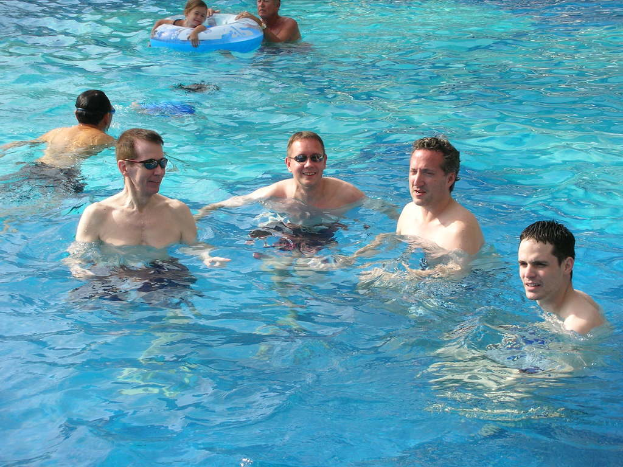 Mehrere Männer schwimmen im Wasser, wobei ein Mädchen ein Ballon-Schwimmen durchführt und eine andere Person den Ballon hält.