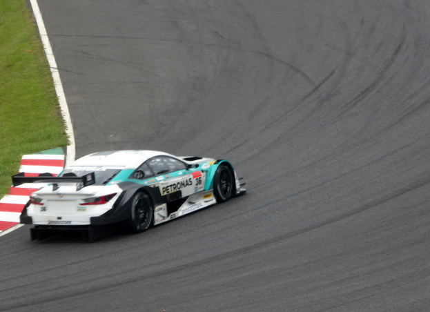 Ein Mercedes-AMG GT3 Rennauto, das auf einer Rennstrecke fährt, mit Text auf dem Auto und Gras auf der linken Seite der Strecke.