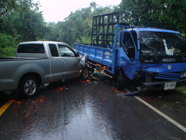 Ein schwer beschädigtter Lkw mit eingedrückter Front und verbeulter Karosserie liegt am Straßenrand, umgeben von Bäumen unter einem klaren blauen Himmel.