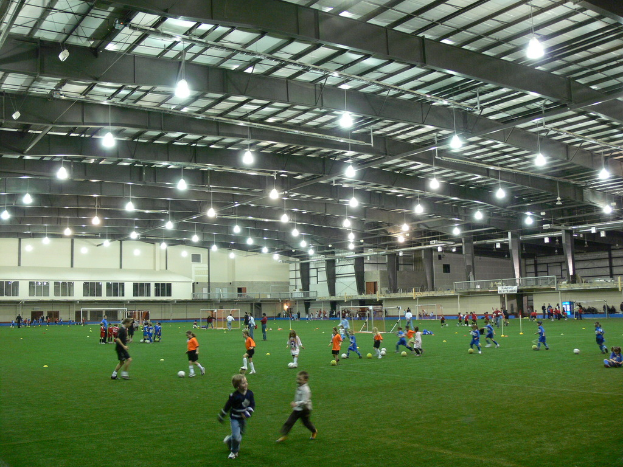 Ein Hallenfußballstadion mit einer Gruppe von Menschen, die mit einem Fußball auf dem Boden spielen, Torpfosten und einer Beleuchtung auf dem Dach.